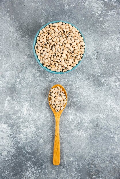 Bowl of white kidney beans with spoon on marble table.