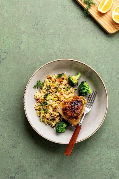 Bowl with chicken pasta orzo with vegetables in Mediterranean style on a green background