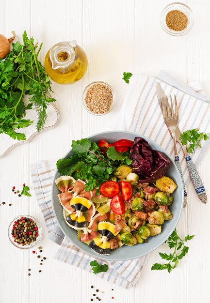 Bowl with Farfalle pasta, Brussels sprouts with bacon and fresh vegetable salad. Flat lay. Top view