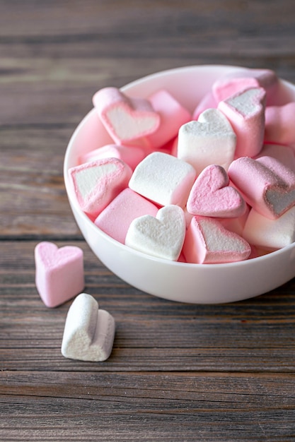 Free photo bowl with marshmallows in the form of hearts closeup on a wooden background