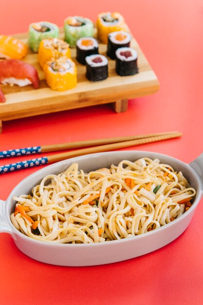 Bowl with noodles near chopsticks and sushi