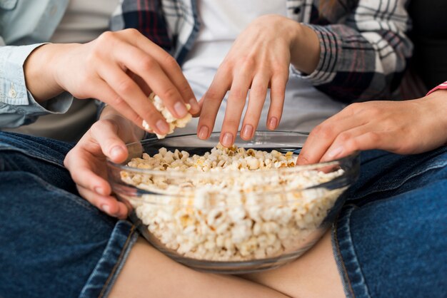 Bowl with popcorn in hands of girl sitting cross-legged on sofa