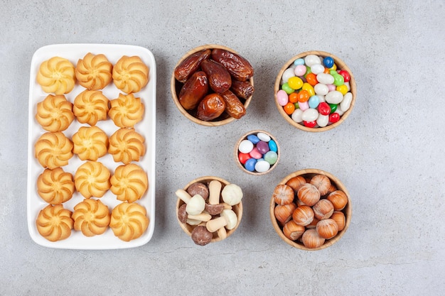 대리석 배경에 접시에 쿠키 옆 사탕, 헤이즐넛, 날짜 및 초콜릿 버섯의 그릇. 고품질 사진