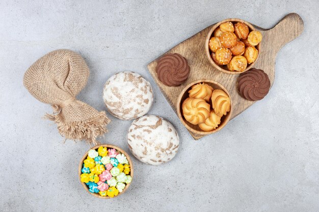 Миски печенья рядом с коричневым печеньем на деревянной доске с русскими сладостями, мешком и миской конфет на мраморной поверхности.