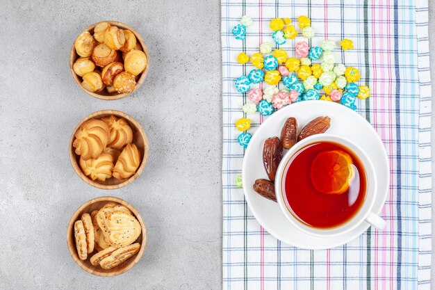 Чаши печенья и чая с финиками и конфетами на мраморной поверхности.
