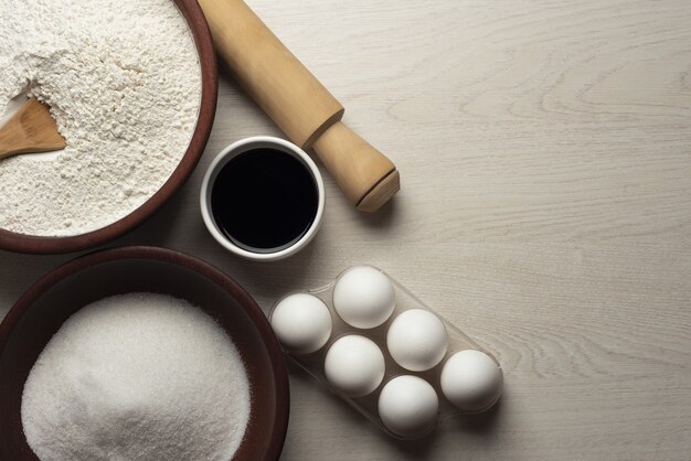 Bowls full of flour, sugar and sauce, some eggs and a rolling pin