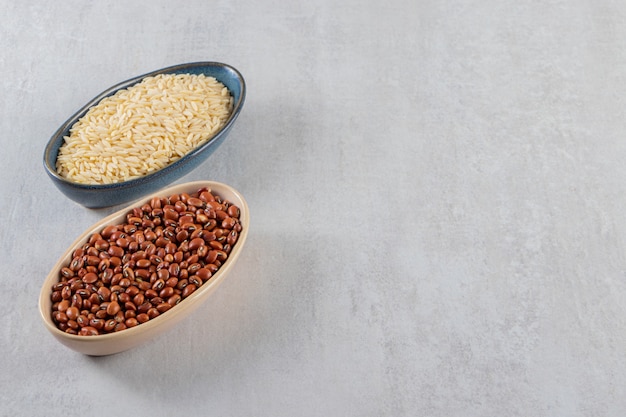 Bowls full of raw beans and long rice on stone table.