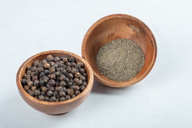 Bowls of grain peppers and ground pepper on white surface.