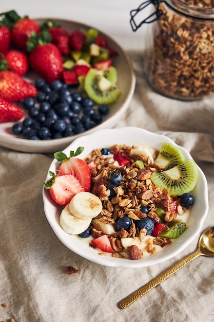 Bowls of granola with yogurt, fruits and berries on a white surface