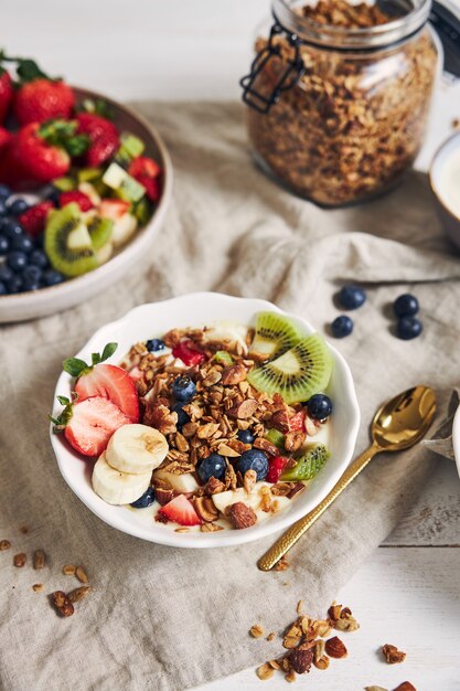 Bowls of granola with yogurt, fruits and berries on a white surface