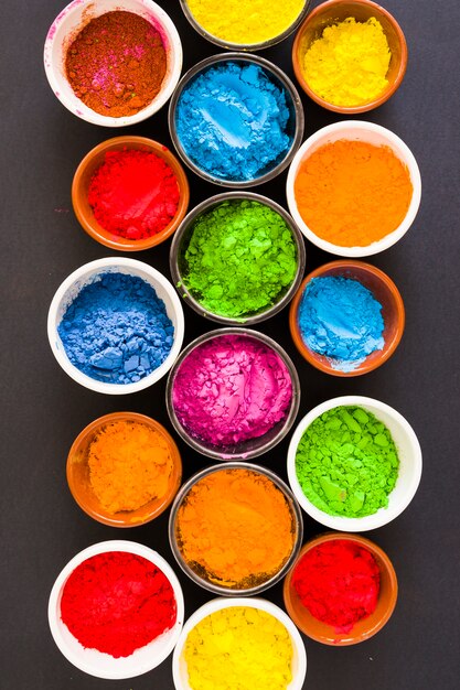 Bowls of holi color powder on black background