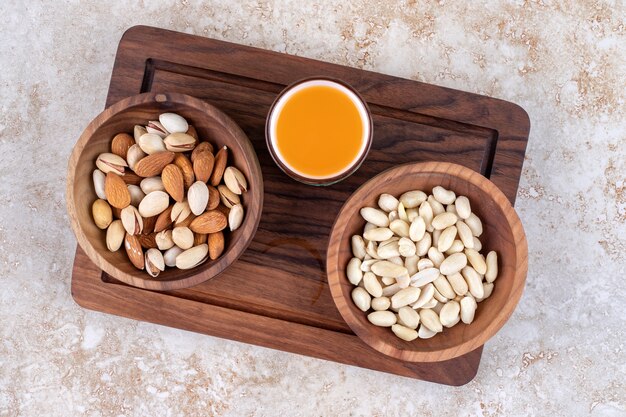 Bowls of nuts and a cup of juice on a board 