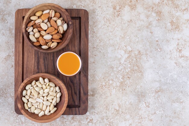 Bowls of nuts and a cup of juice on a board 