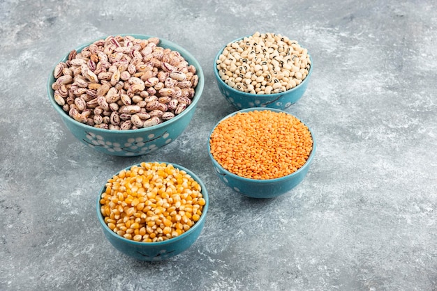 Бесплатное фото Миски сырых бобов, чечевицы и кукурузы на мраморной поверхности.