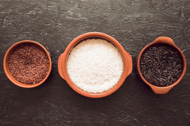 Bowls of organic rice grains on gray textured background