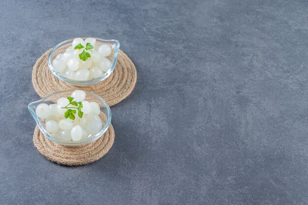 Bowls of pickled baby onion on trivet on the marble surface