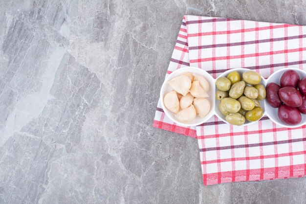 Bowls of pickled plums, olives and garlic on tablecloth.