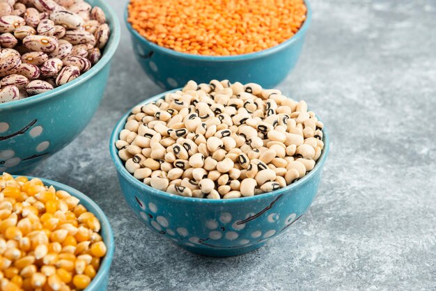 Bowls of raw beans, lentils and corns on marble surface.