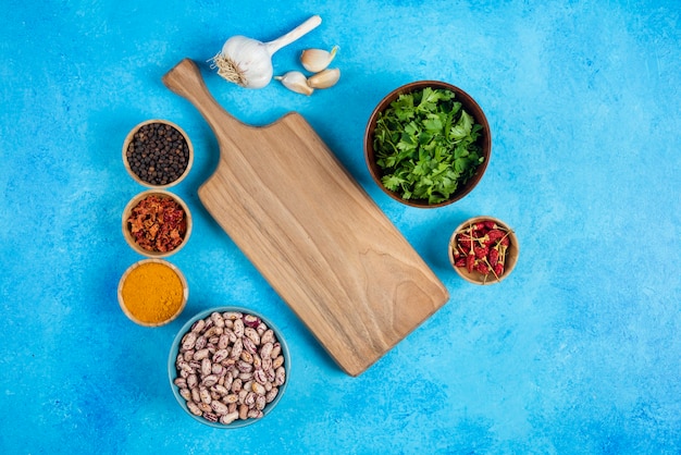 Bowls of raw beans and organic spices on blue background.