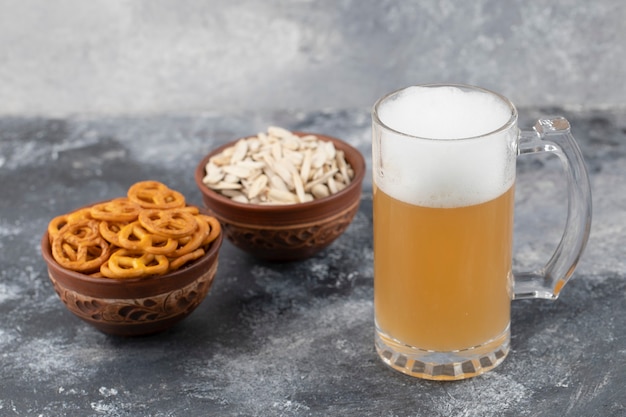 Bowls of salted pretzels and sunflower seeds with mug of beer on marble surface