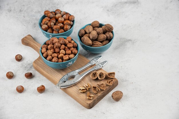 Bowls of walnuts, hazelnuts and kernels on wooden cutting board. 