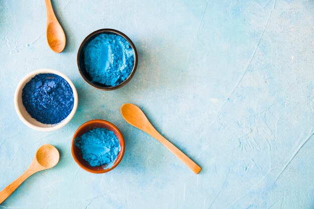 Bowls with holi color powder and wooden spoon on painted background