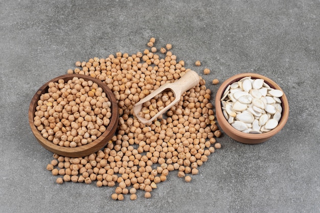 Bowls of yellow peas and pumpkin seeds on marble.