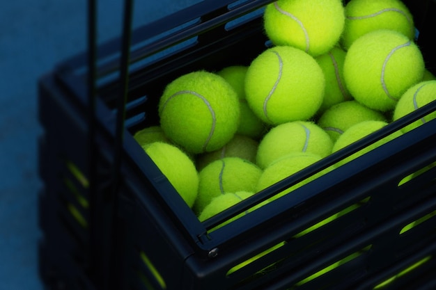 Free photo box full of tennis balls is standing on the floor at tennis court.