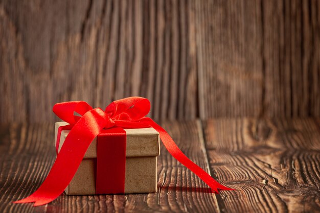 Box of present with red ribbon bow on wooden background