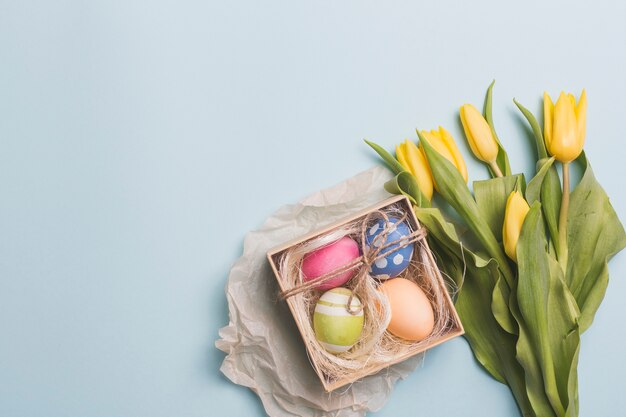 Box with eggs near tulips on blue