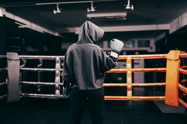 Boxer girl with hoodie and boxing gloves on standing in ring with backs turned. one hand lifted up. Premium Photo
