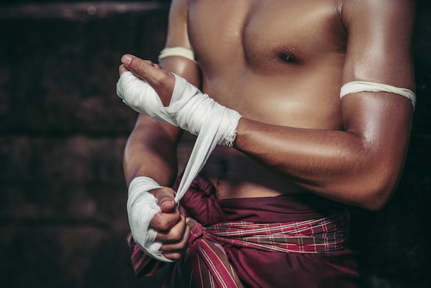 Free photo the boxer sat on the stone, tied the tape around his hand, preparing to fight.