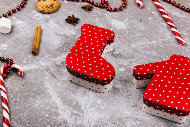 Boxes in form of Christmas socks and sweater lie on grey floor surrounded with cookies, spices and red white candies