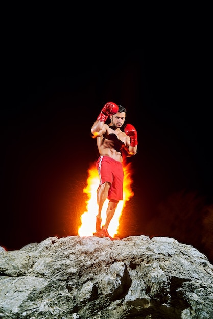 Boxing champion posing on top of a rock with fire burning on the