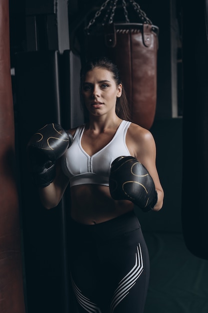 Бокс женщина позирует с боксерской грушей, на темном фоне. Сильная и независимая концепция женщины