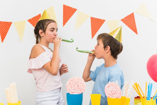 Бесплатное фото Мальчик и девочка дует рога во время дня рождения