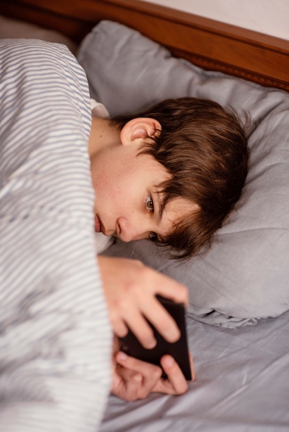 Foto gratuita ragazzo a letto che gioca sul cellulare