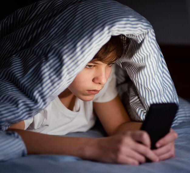Мальчик в постели, играя на мобильном телефоне