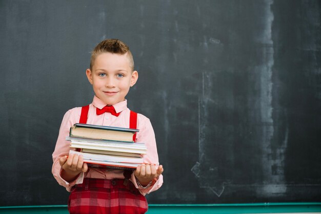 Boy at blackboard with books stack