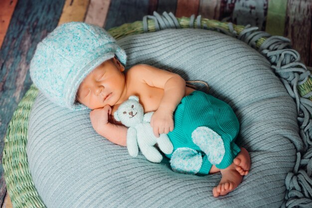 Boy in blue large hat sleeps with bear on pillow 