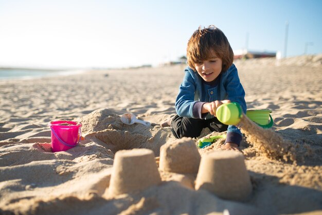 Boy building sandcastle. Schoolboy playing on beach on summer holidays