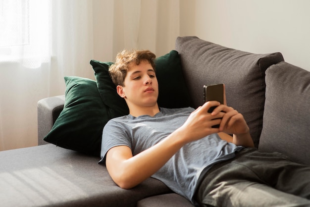 Foto gratuita ragazzo che controlla il suo telefono a casa