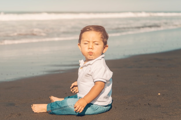 Boy closing eyes while sitting on sandy beach