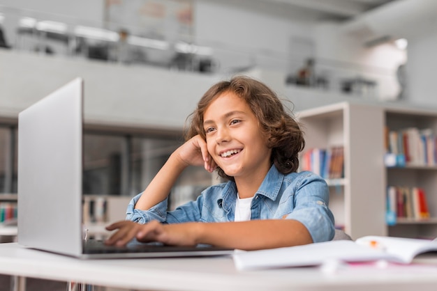 Foto gratuita ragazzo che fa i compiti su un laptop in biblioteca