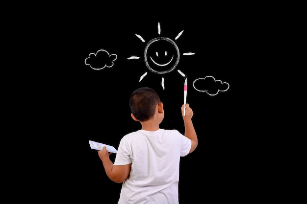 A boy draws the sky and the sun with a chalkboard