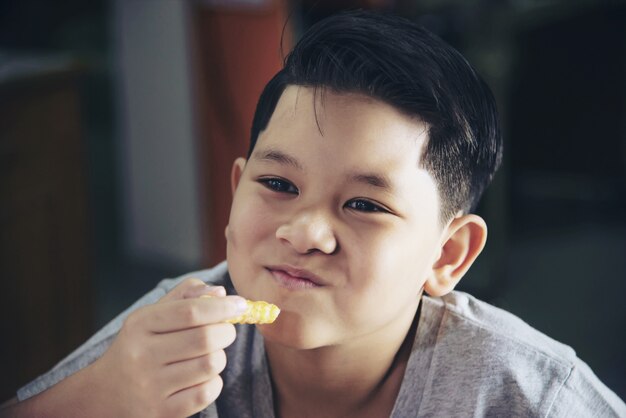 Мальчик ест картофель фри с соусом на белом деревянном столе