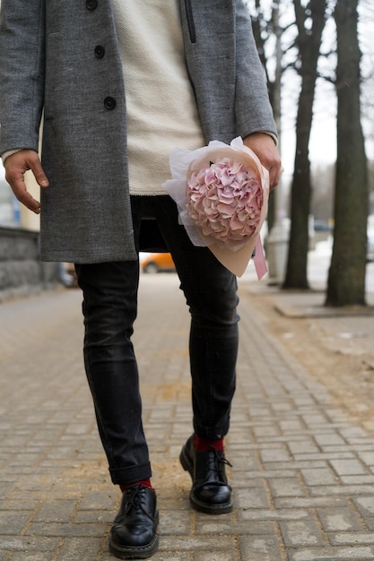 Boy friend with a bouquet of pink flowers hydrangea waiting for his girl friend outdoors while snow is falling. Valetnine`s day concept, wedding proposal. 
man goes on a date.