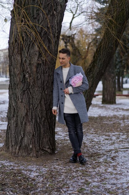 Друг парня с букетом розовых цветов гортензии ждет свою подругу на улице, пока идет снег. Концепция дня святого валентина, свадебное предложение. мужчина идет на свидание.