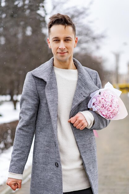 雪が降っている間、屋外で彼のガールフレンドを待っているピンクの花アジサイの花束を持つボーイフレンド。 Valetnineの日のコンセプト、プロポーズ。男はデートに行きます。