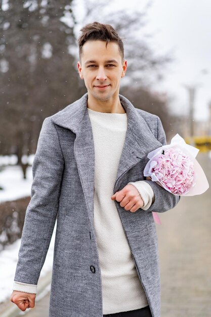 Друг парня с букетом розовых цветов гортензии ждет свою подругу на улице, пока идет снег. Концепция дня святого валентина, свадебное предложение. мужчина идет на свидание.